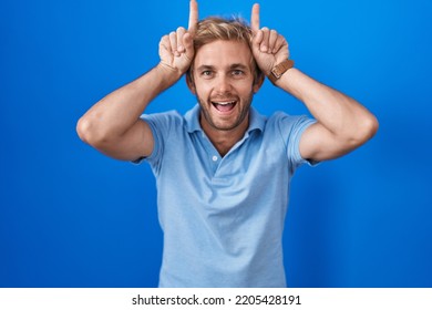 Caucasian Man Standing Over Blue Background Doing Funny Gesture With Finger Over Head As Bull Horns 