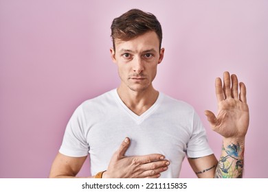 Caucasian Man Standing Over Pink Background Swearing With Hand On Chest And Open Palm, Making A Loyalty Promise Oath 