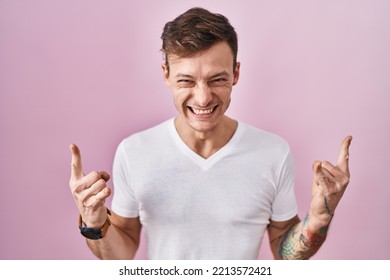 Caucasian Man Standing Over Pink Background Shouting With Crazy Expression Doing Rock Symbol With Hands Up. Music Star. Heavy Music Concept. 