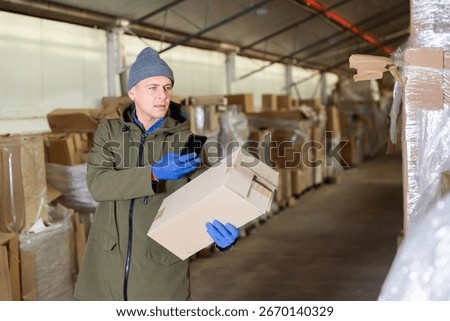 Caucasian man storekeeper using his phone to take photograph of pasteboard box.