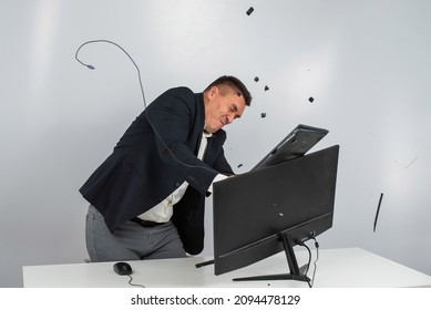 Caucasian man in a suit gets angry and smashes the keyboard on the monitor. An office worker in a rage breaks the computer. - Shutterstock ID 2094478129