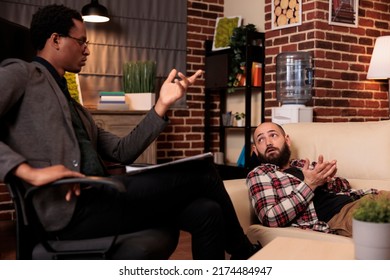 Caucasian Man Talking To Male Counselor About Psychological Issues, Laying On Couch At Therapy Session. Receiving Counseling Advice And Support From Therapist, Doing Psychoanalysis.