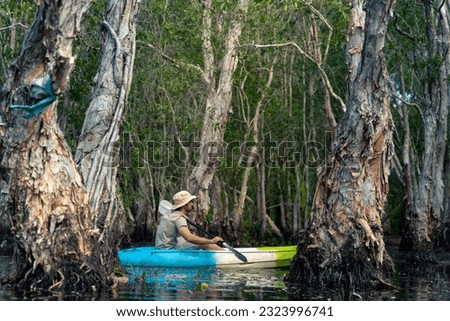 Caucasian man tourist enjoy outdoor lifestyle kayaking at mangrove forest on summer vacation. Handsome guy traveler canoeing or row the boat on lake. Environmental ecotourism and solo travel concept.