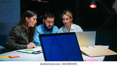 Caucasian man and two women working late at night in office and watching something on tablet device. Businessman and businesswomen having meeting and brainstorming discussion. - Powered by Shutterstock