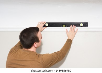 Caucasian Man Uses Bubble Level To Level White Wood Trim Crown Moulding During Installation