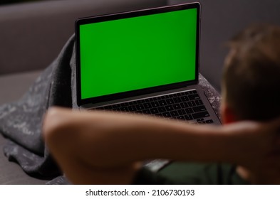 Caucasian Man Uses Laptop With Greenscreen Of Chromakey Mockup. Person Watches The Video, Relaxes, Enjoys The Rest On Personal Computer. Green Screen And Chroma Key.