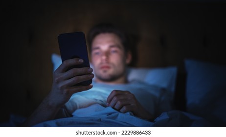 Caucasian Man Uses Smartphone in Bed at Home at Night. Handsome Guy Browsing Social Media, Reading News, Doing Online Shopping, Chatting with Friends Late at Night. - Powered by Shutterstock