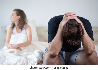 Caucasian man wearing black shirt on bed with angry wife, feeling disappointed and depressed because of erectile dysfunction.