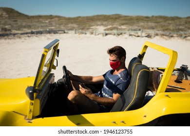 Caucasian Man Wearing Face Mask Sitting In Beach Buggy Using Smartphone. Beach Stop Off On Summer Holiday Road Trip During Coronavirus Covid 19 Pandemic.