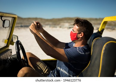 Caucasian Man Wearing Face Mask Sitting In Beach Buggy Taking Picture. Beach Stop Off On Summer Holiday Road Trip During Coronavirus Covid 19 Pandemic.