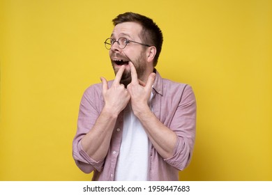 Caucasian man wearing glasses and casual clothes opened his mouth and shows missing tooth. Isolated, yellow background.