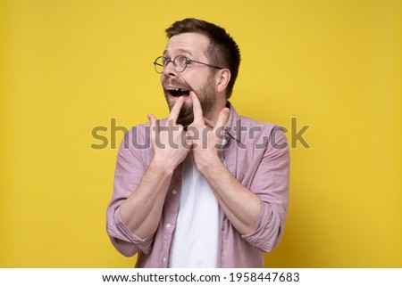 Caucasian man wearing glasses and casual clothes opened his mouth and shows missing tooth. Isolated, yellow background.