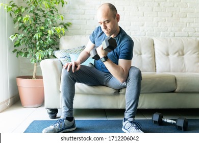 Caucasian Man Wearing A Smartwatch Sitting In A Sofa At Home And Doing Bicep Curls And Lifting Weights