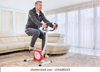 Caucasian Man Wearing Sportswear While Training With A Spin Bike In The Living Room. Shot At Home