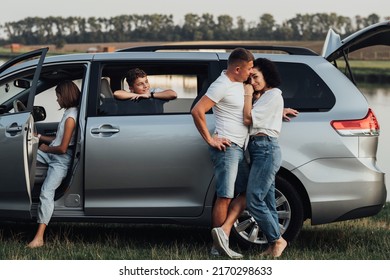 Caucasian Man and Woman Hugging Near the Minivan Car, Happy Four Members Family Enjoying Road Trip, Making Stop by River