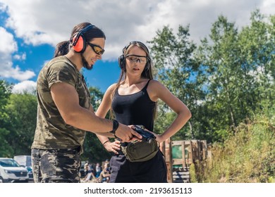 Caucasian Man And Woman Wearing Safety Goggles And Headphones Learning How To Operate Handgun. Firearms Training At Firing Range. Horizontal Outdoor Shot. High Quality Photo