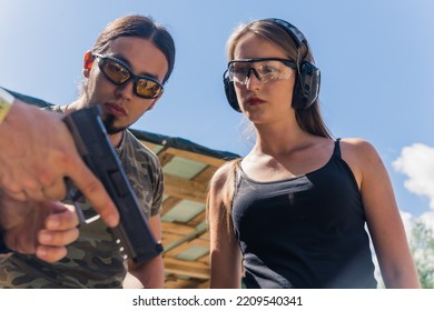 Caucasian Man And Woman Wearing Safety Goggles Listening To Instructor Showing How To Operate Handgun. Firearms Training. Horizontal Shot. High Quality Photo