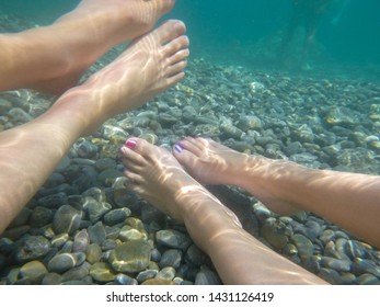 Caucasian Man And Women With Purple And Pink Painted Toe Nails Relaxing With Her Feet Floating Under The Water In The Mediterranean Sea. Light Reflects Through The Water. Concept Holiday Background.