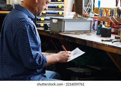 Caucasian Man Working In Workshop With Old Tools Hanging On Wall In Workshop, Tool Shelf Against A Table And Wall, Vintage Garage Style.