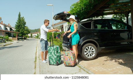 Caucasian Man Yells In The Sunny Driveway At Laughing Girlfriend For Packing Too Much Luggage For Their Summer Vacation. Young Caucasian Newlywed Couple Arguing And Overpacking Before Their Honeymoon.