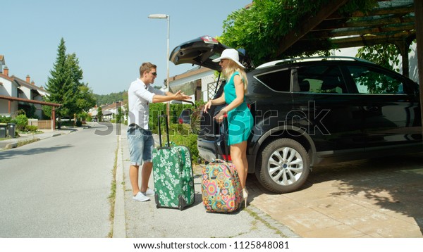 Caucasian man yells in the sunny driveway at\
laughing girlfriend for packing too much luggage for their summer\
vacation. Young Caucasian newlywed couple arguing and overpacking\
before their\
honeymoon.