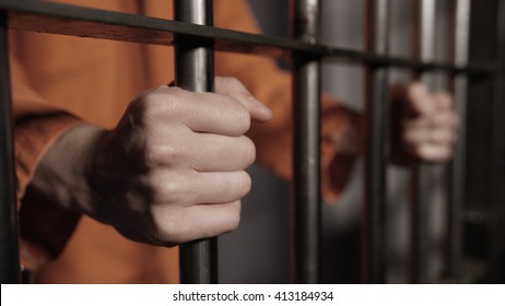 Caucasian man's hands on the bars of a prison cell