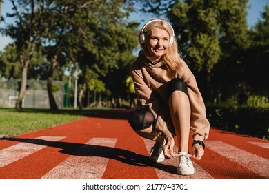 Caucasian mature female runner athlete tying training shoes while jogging on the stadium in public park in the morning. Active healthy sporty lifestyle. - Powered by Shutterstock