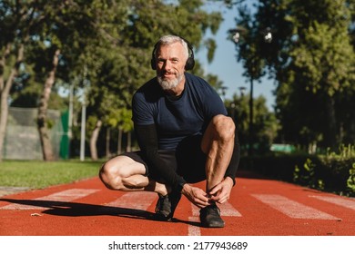 Caucasian mature male runner athlete tying training shoes while jogging on the stadium in public park in the morning. Active healthy sporty lifestyle. - Powered by Shutterstock