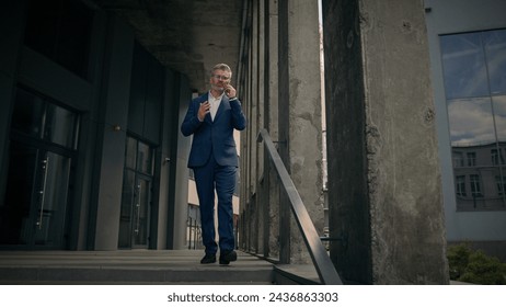 Caucasian mature old man businessman senior business employer walking outdoors on stairs near office building talking phone check time looking at wrist watch late rush hurry worried running lateness - Powered by Shutterstock