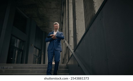 Caucasian mature old man businessman senior business employer walking outdoors on stairs near office building talking phone check time looking at wrist watch late rush hurry worried running lateness - Powered by Shutterstock