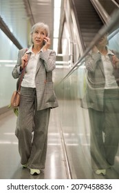 Caucasian Mature Woman Talking On Phone While Walking Inside Office Building Near Escalator.