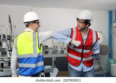 Caucasian Mechanic Technician Maintenance, Repairing Industrial Machinery Equipment In Factory. Worker In Protective Clothing With Goggles And Mask Making Elbow Bump Greeting At Manufacturing Factory