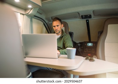 Caucasian Men In His 40s Working On His Computer Straight From His Camper Van While On A Road Trip. Remote Working Theme.