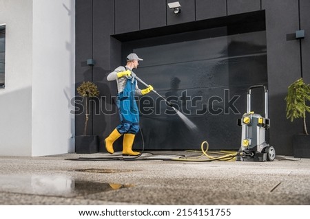 Caucasian Men Pressure Washing His Garage Gate Using Powerful Washer. Keeping the Gate and Driveway Clean. 