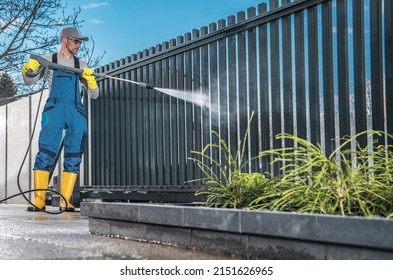 Caucasian Men Washing His Residential Driveway Gate Using Pressure Washer. Home Surrounding Maintenance.