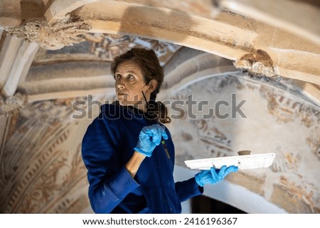 Caucasian Mid Adult Woman Restorer Retouching Antique Gothic Fresco on Church Ceiling