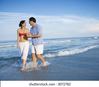 Caucasian mid-adult couple holding hands wading in ocean. - Powered by Shutterstock