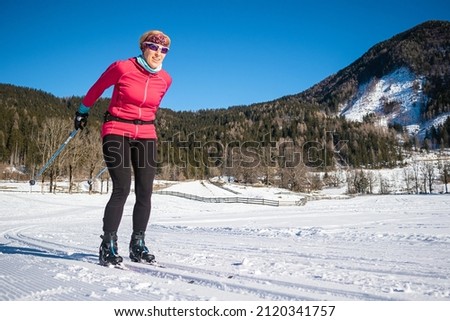 Caucasian middle aged woman, in ski wear and gear cross country style skiing.