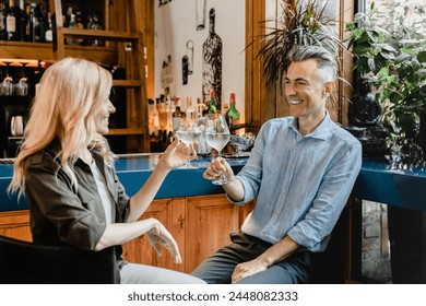 Caucasian middle-aged couple drinking sparkling wine cocktails together on a romantic date relaxing at the bar counter in cafe restaurant together. - Powered by Shutterstock