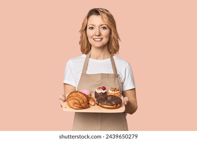 Caucasian middle-aged female baker with sweets tray in studio - Powered by Shutterstock