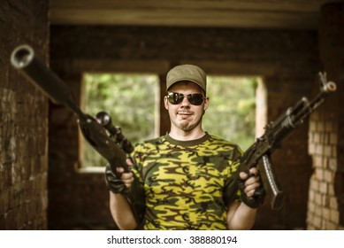 Caucasian Military Man With Black Sunglasses Indoor Urban Room Space Stand With A Kalashnikov Rifle Near Abandoned Red Brick Wall With Windows. Corridor In Perspective.Empty Space For Inscription