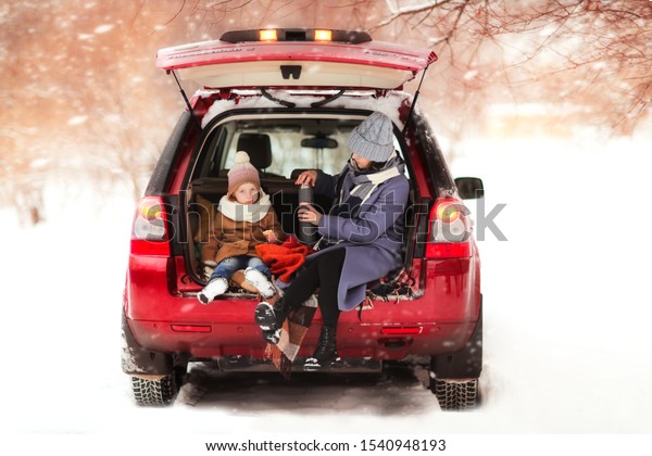 Caucasian mom with a daughter with a thermos in
the trunk of a car, winter travel with children and a picnic in a
car in winter, toning