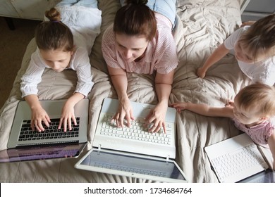 Caucasian Mom And Three Siblings Children Lie On The Bed With Laptops, Concept Digital Addiction, Home, Distance Learning Online, Mother Works Remotely With Children.