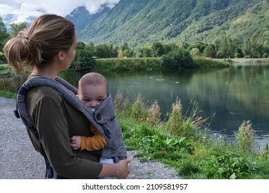 Caucasian Mother With A Baby Carrier Taking A Walk Around A Lake In The Middle Of Nature. Healthy Lifestyle