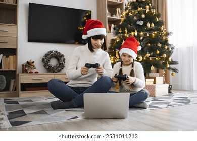 Caucasian mother and daughter enjoying video games using joysticks and laptop during Christmas. Warm family bonding moment in cozy living room with decorated tree and festive atmosphere. - Powered by Shutterstock