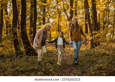 Caucasian mother, daughter and grandmother are walking trough the wood in autumn, exploring and having a great time