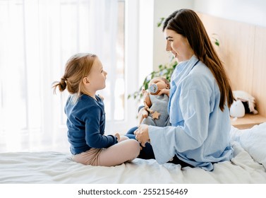 Caucasian mother enjoying cozy morning with her two children at home. Little girl, wearing cozy outfit, having sweet interaction with newborn baby sibling. Bright natural light warm home atmosphere. - Powered by Shutterstock