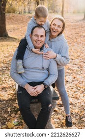 Caucasian Mother, Father And Son Posing Together In The Autumn Park, Smiling To The Camera. Family, Childhood, Real People Lifestyle Concept. Healthy Lifestyle