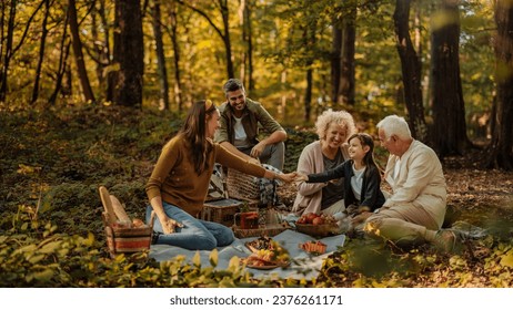 Caucasian mother, father, their daughter and grandparents are all together on a picnic in a forest during fall, having fun and laughing - Powered by Shutterstock