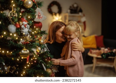 Caucasian mother and her happy daughter are hugging in their home during Christmas, decorating a Christmas tree and having fun - Powered by Shutterstock